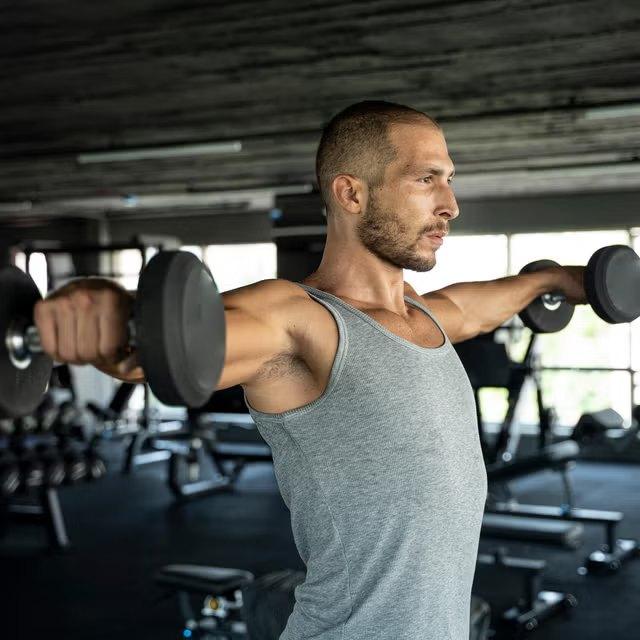 Member working through a set of dumbbell lateral raises on the gym floor